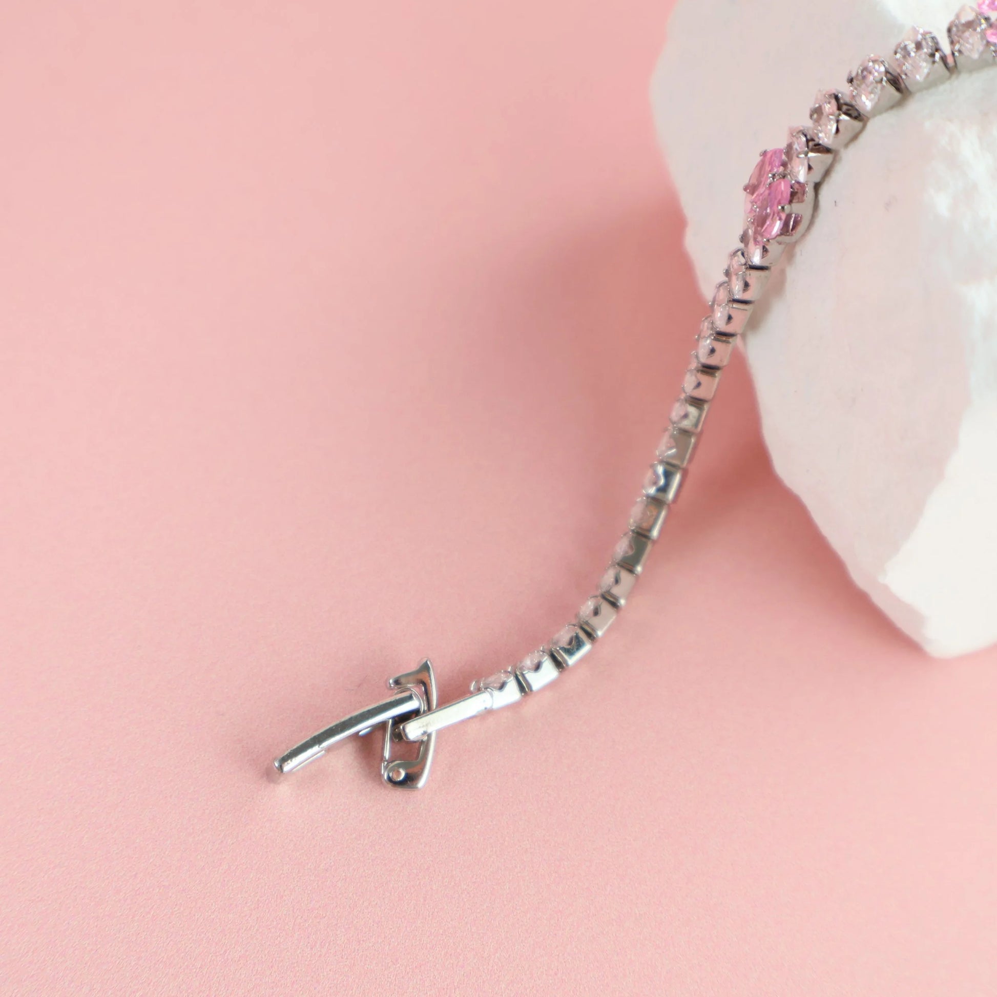 Silver and pink zirconia bracelet displayed on textured white prop